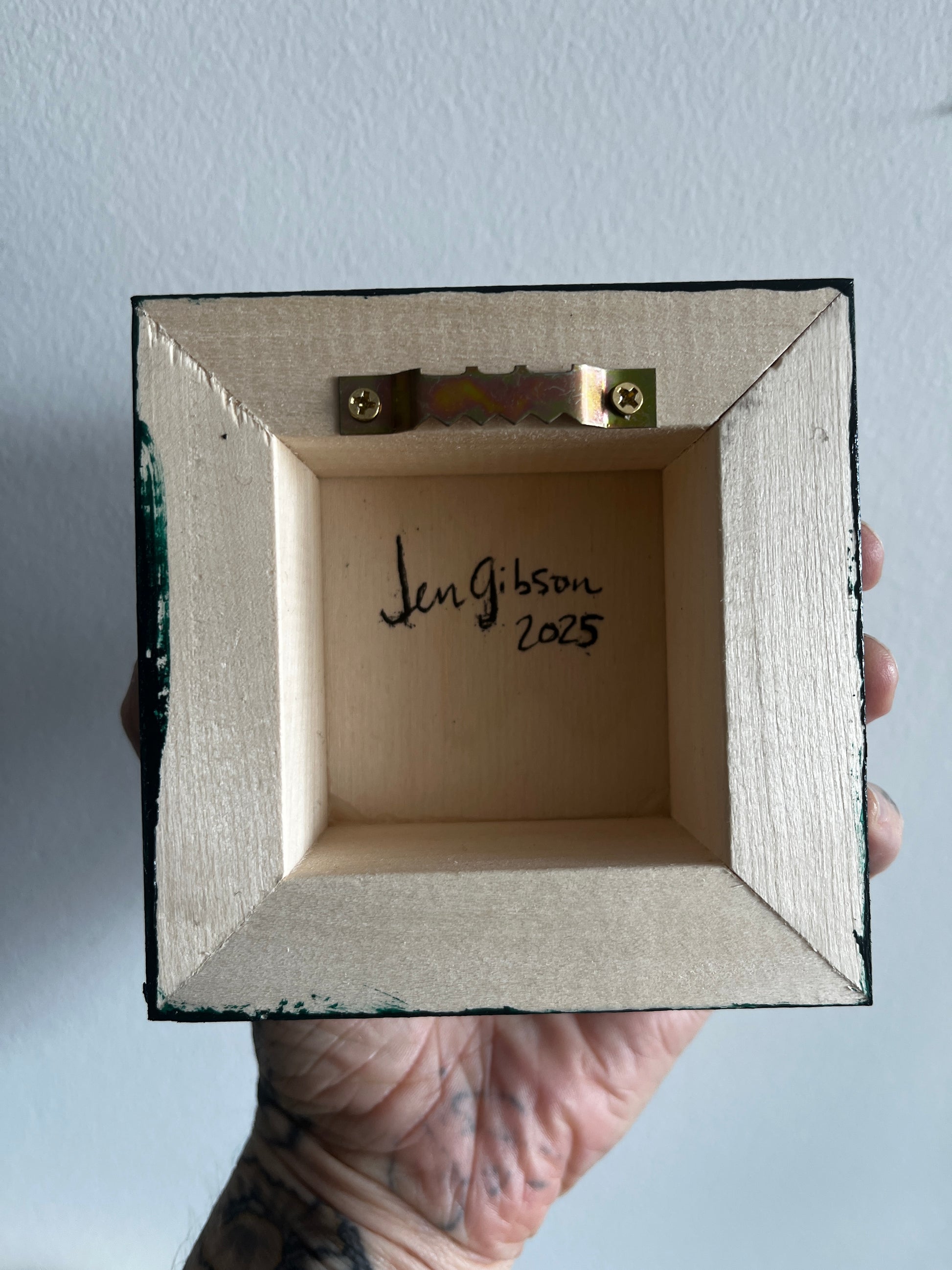 Hand holding a small wooden box with 'Jen Gibson 2023' engraved on a light gray background