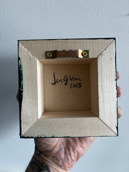 Hand holding a small wooden box with 'Jen Gibson 2023' engraved on a light gray background