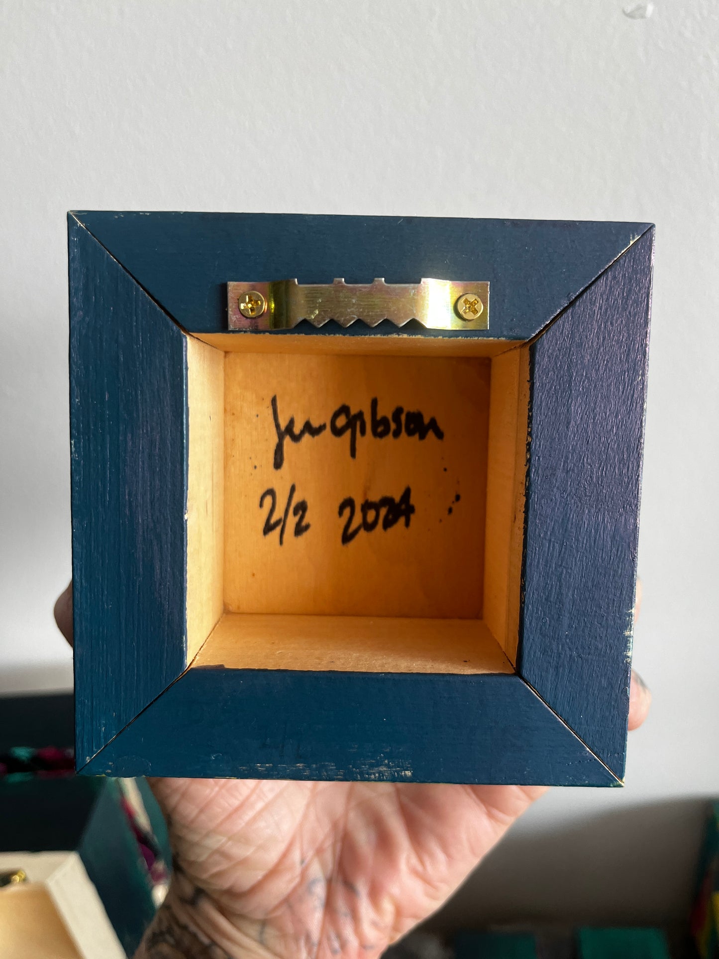 Navy blue wooden box with a gold latch, held by a hand against a neutral background.