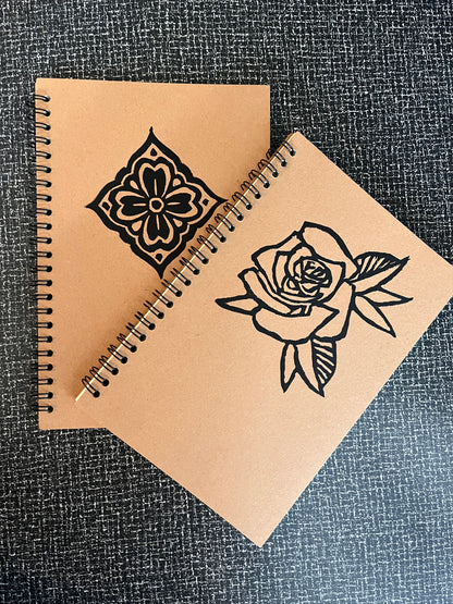 Brown notebook with black floral designs on a textured surface