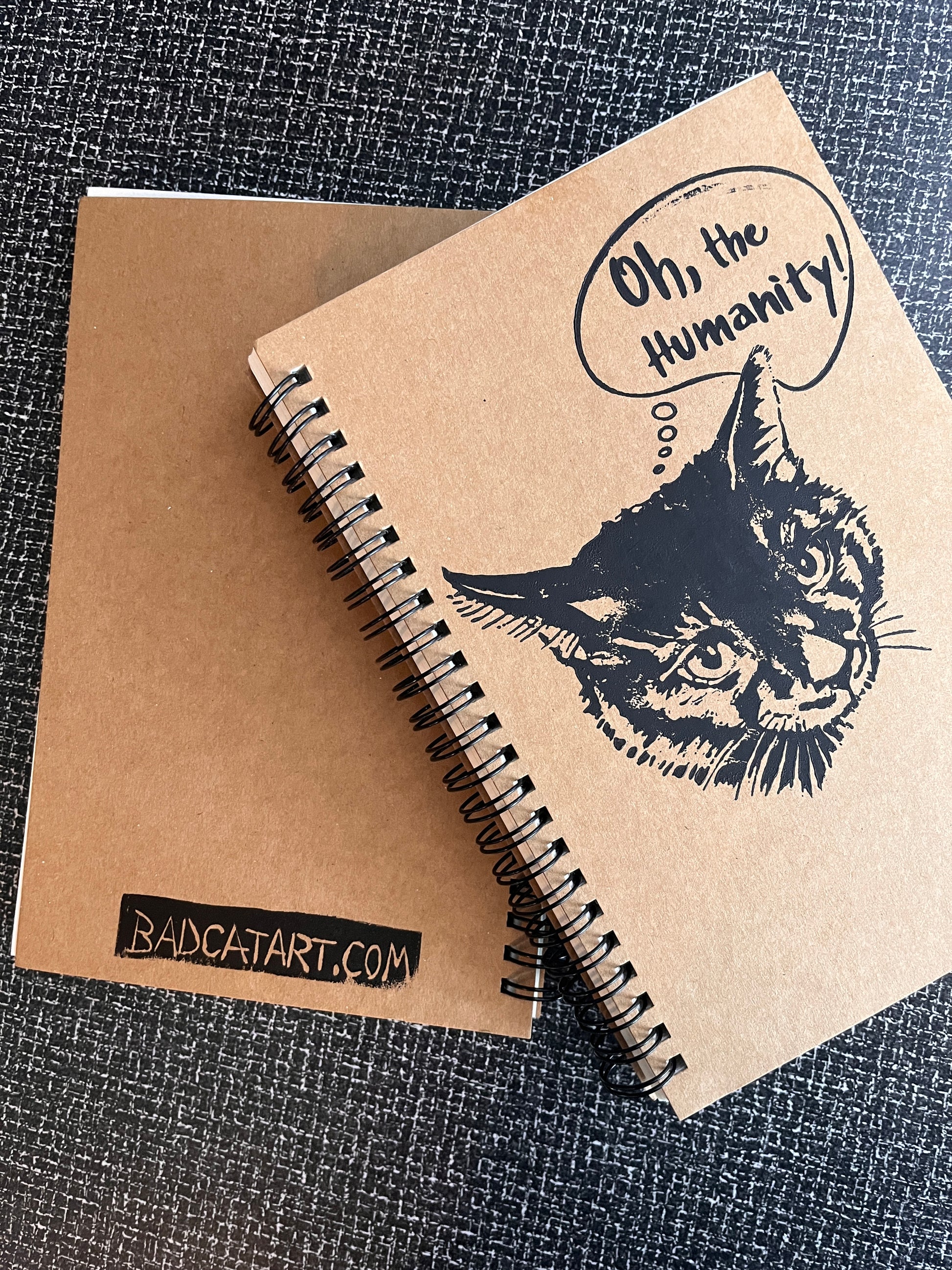 Kraft paper notebook front and reverse views with a printed design of a cat and text on a textured surface