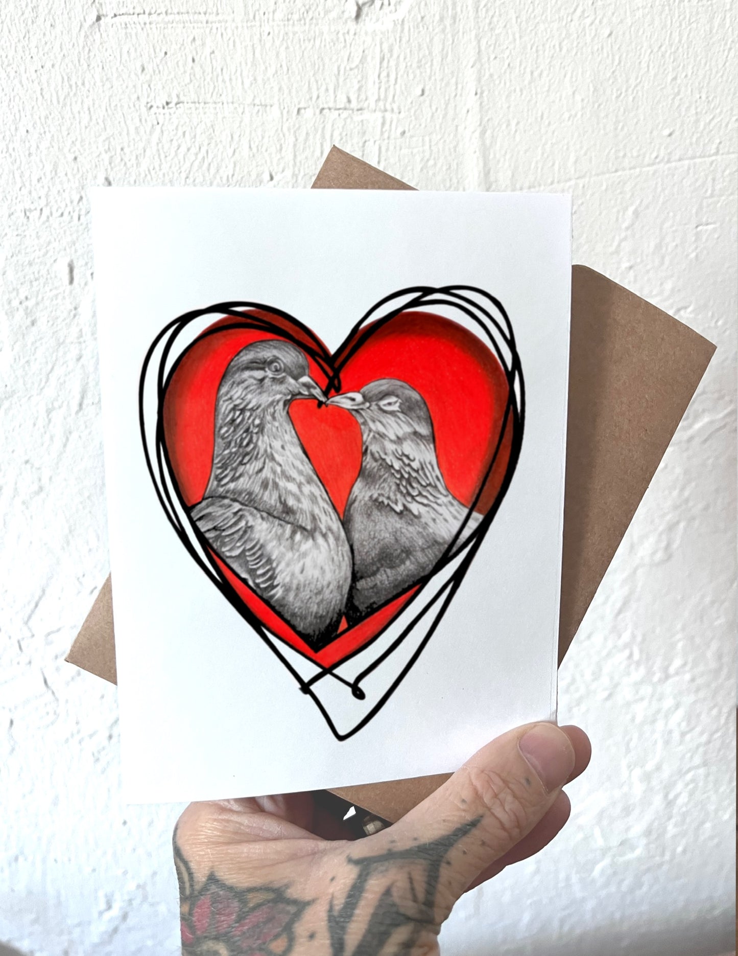 Card with two birds in a heart shape held by a hand against a textured white background