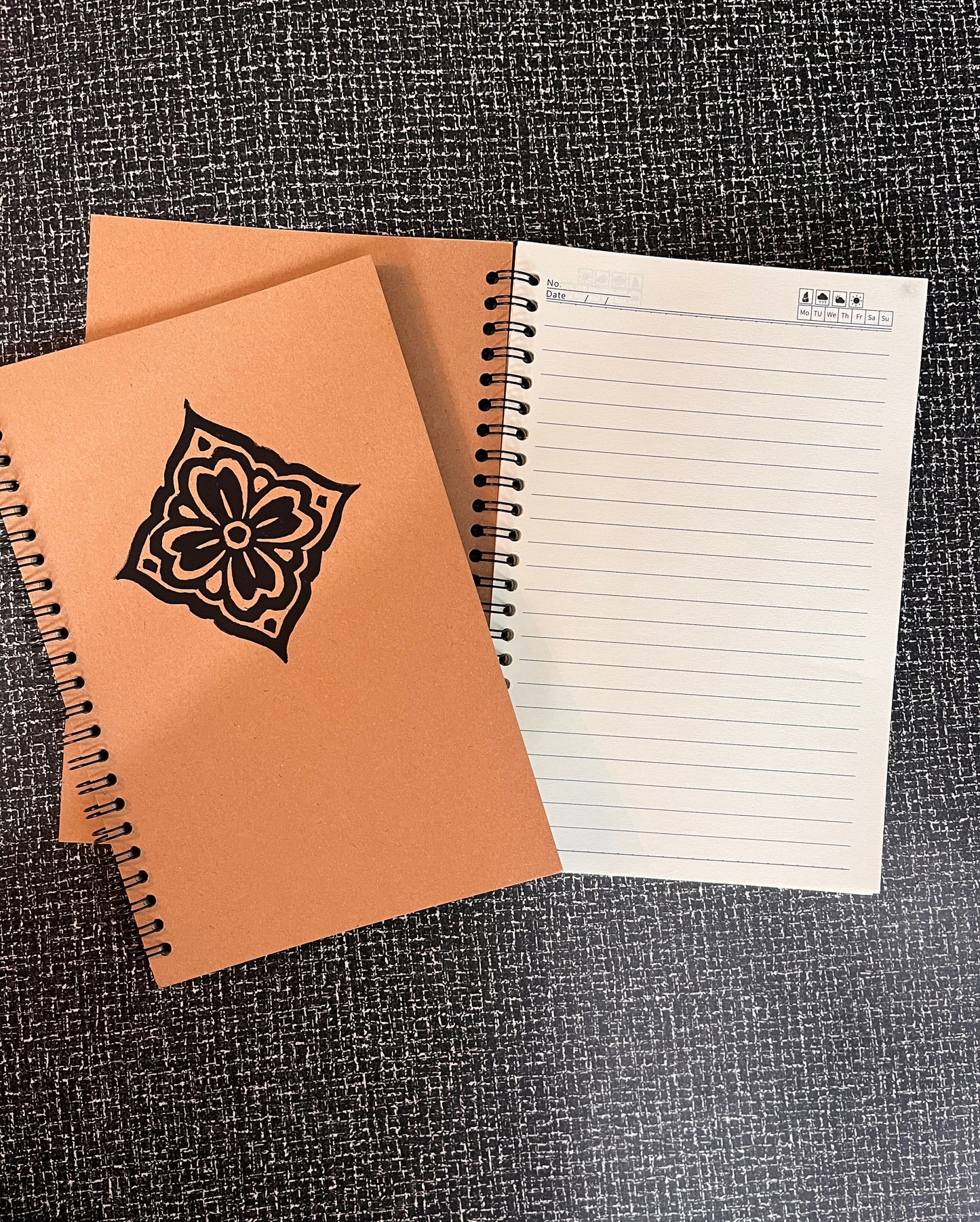 Two notebooks, one with a floral design on the cover, on a textured surface.