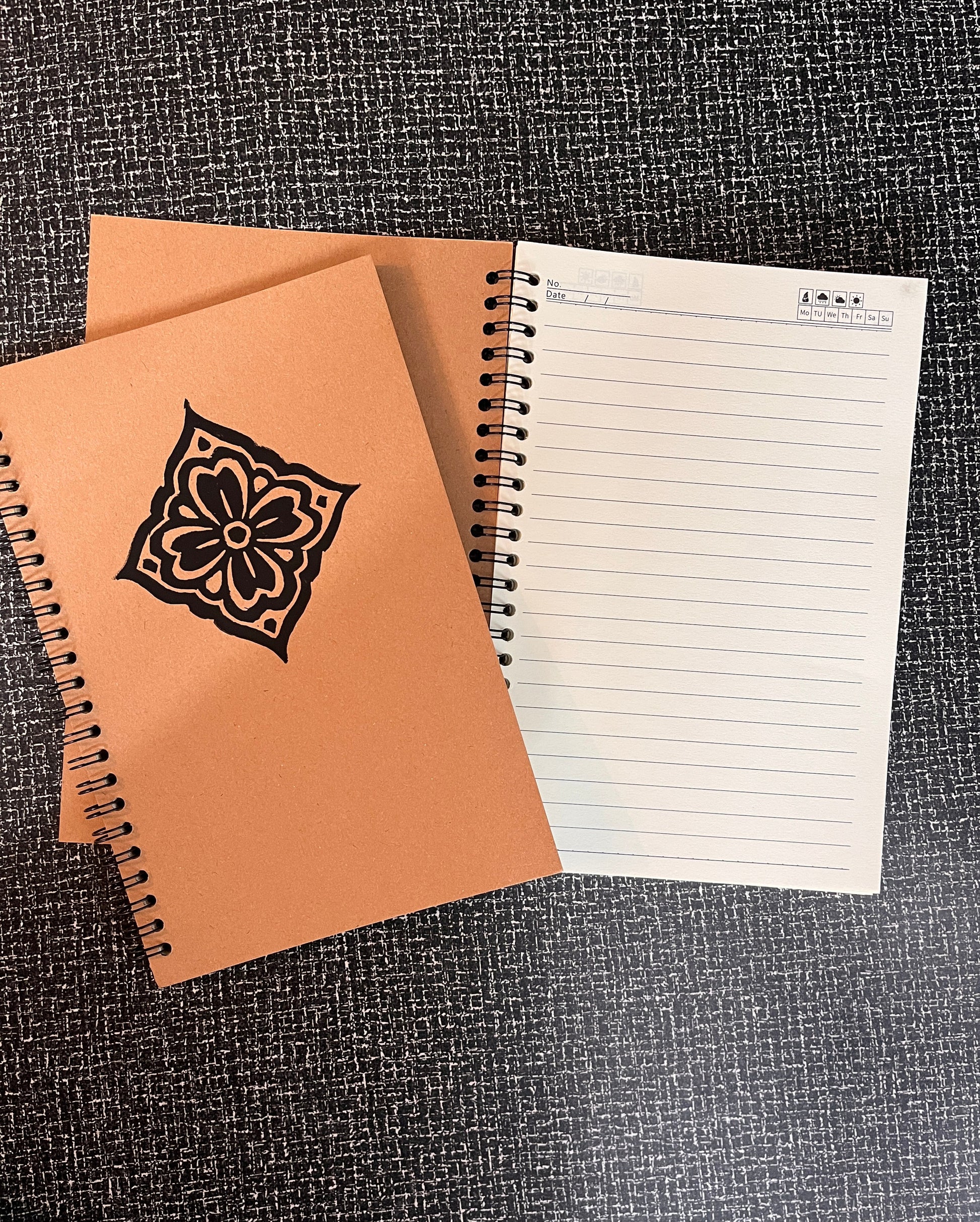 Two notebooks, one with a floral design on the cover, on a textured surface.