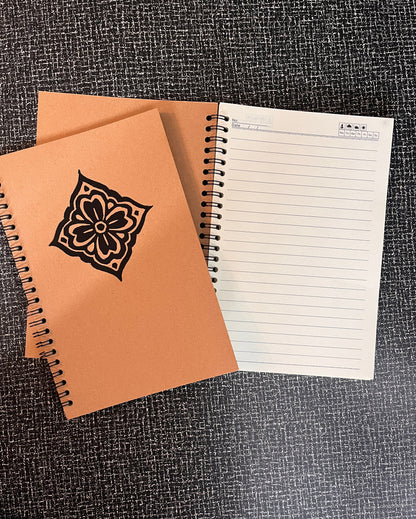 Two notebooks, one with a floral design on the cover, on a textured surface.
