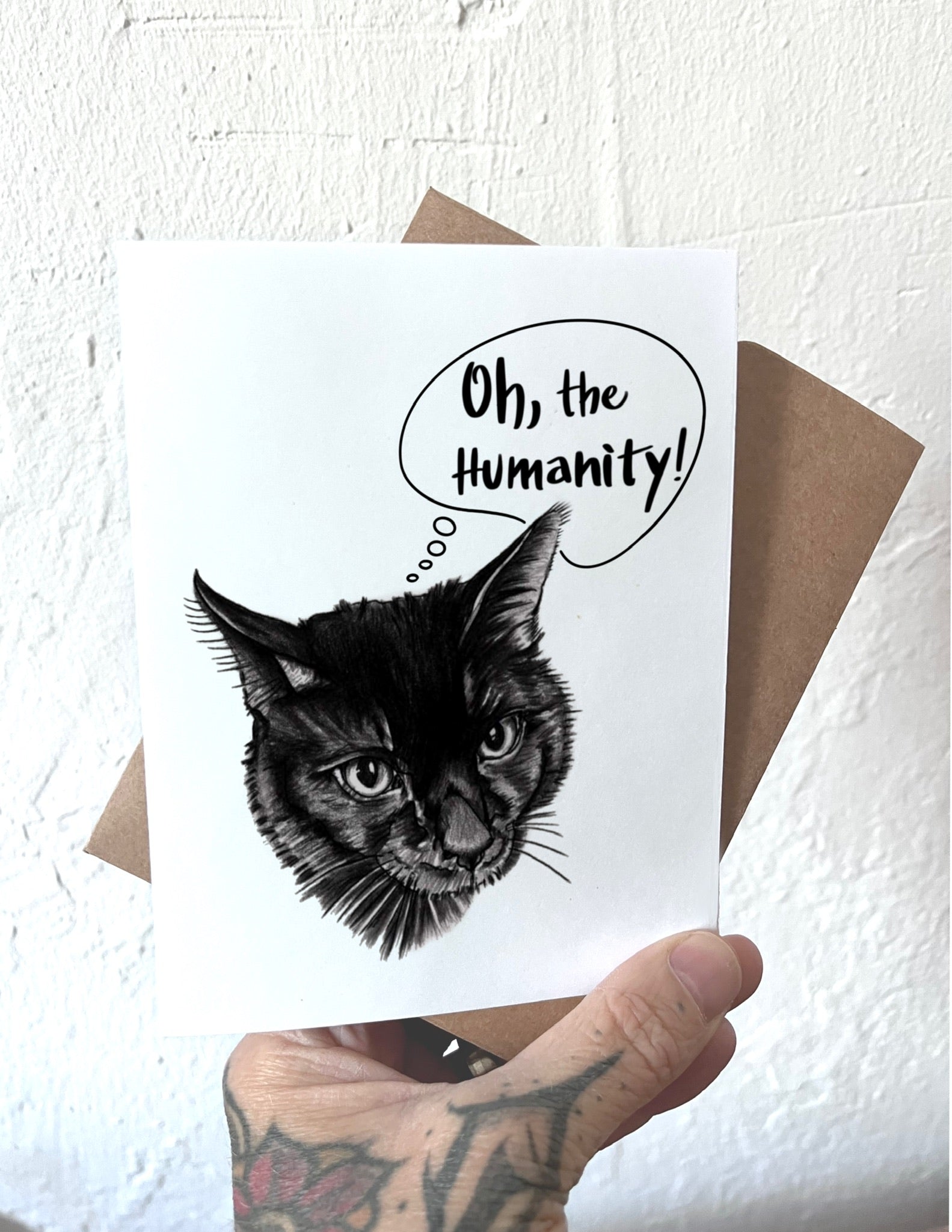 Card with a black cat illustration and 'Oh, the Humanity!' text held by a person.