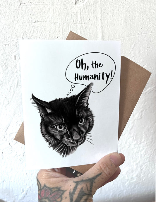Card with a black cat illustration and 'Oh, the Humanity!' text held by a person.