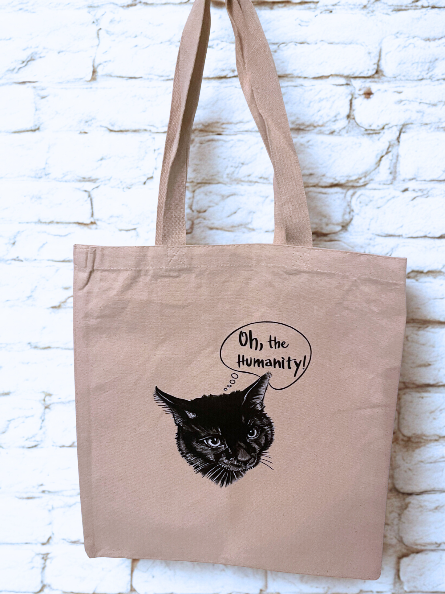 tote bag hanging on brick wall with a black cat on it