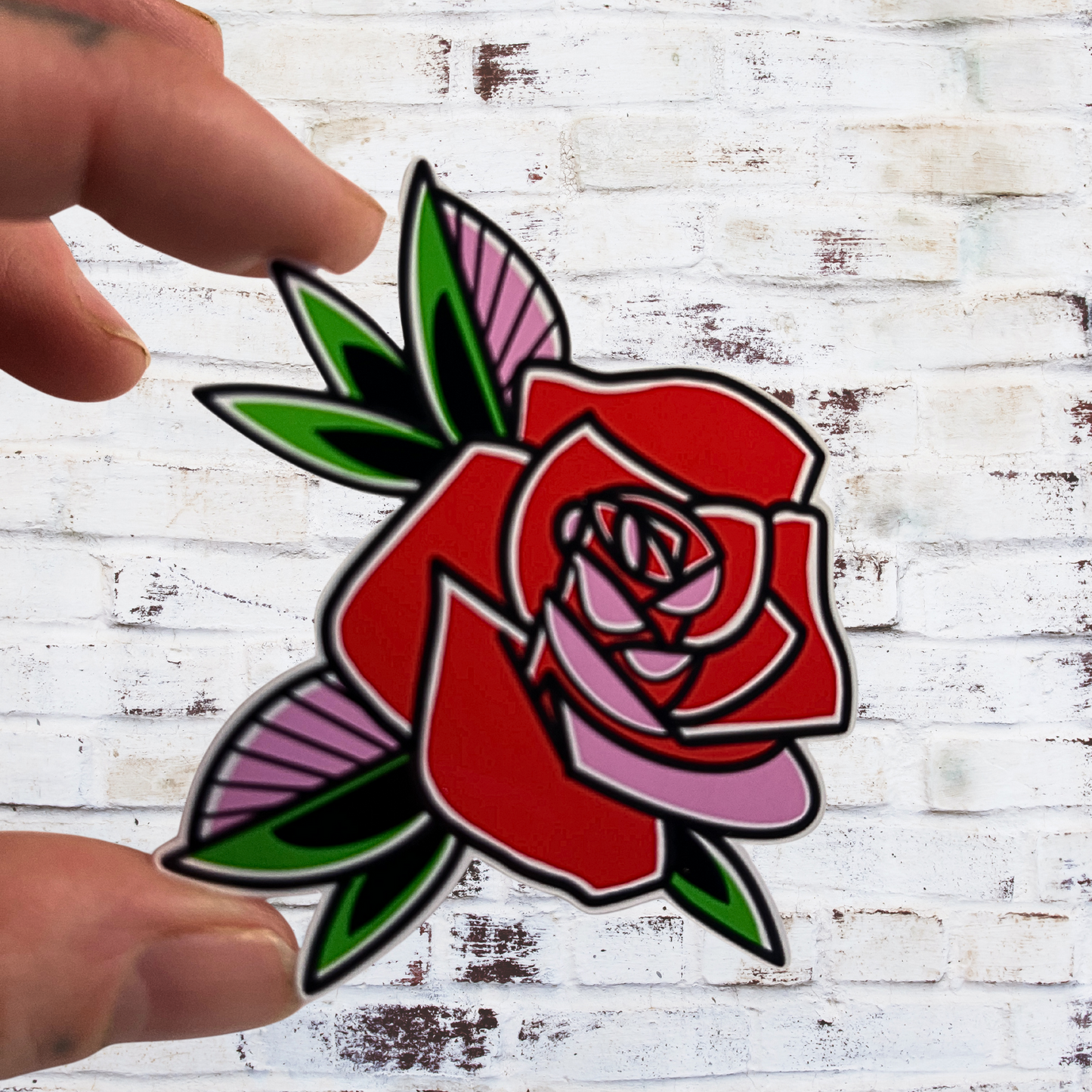 Hand holding a red rose tattoo design against a white wooden background