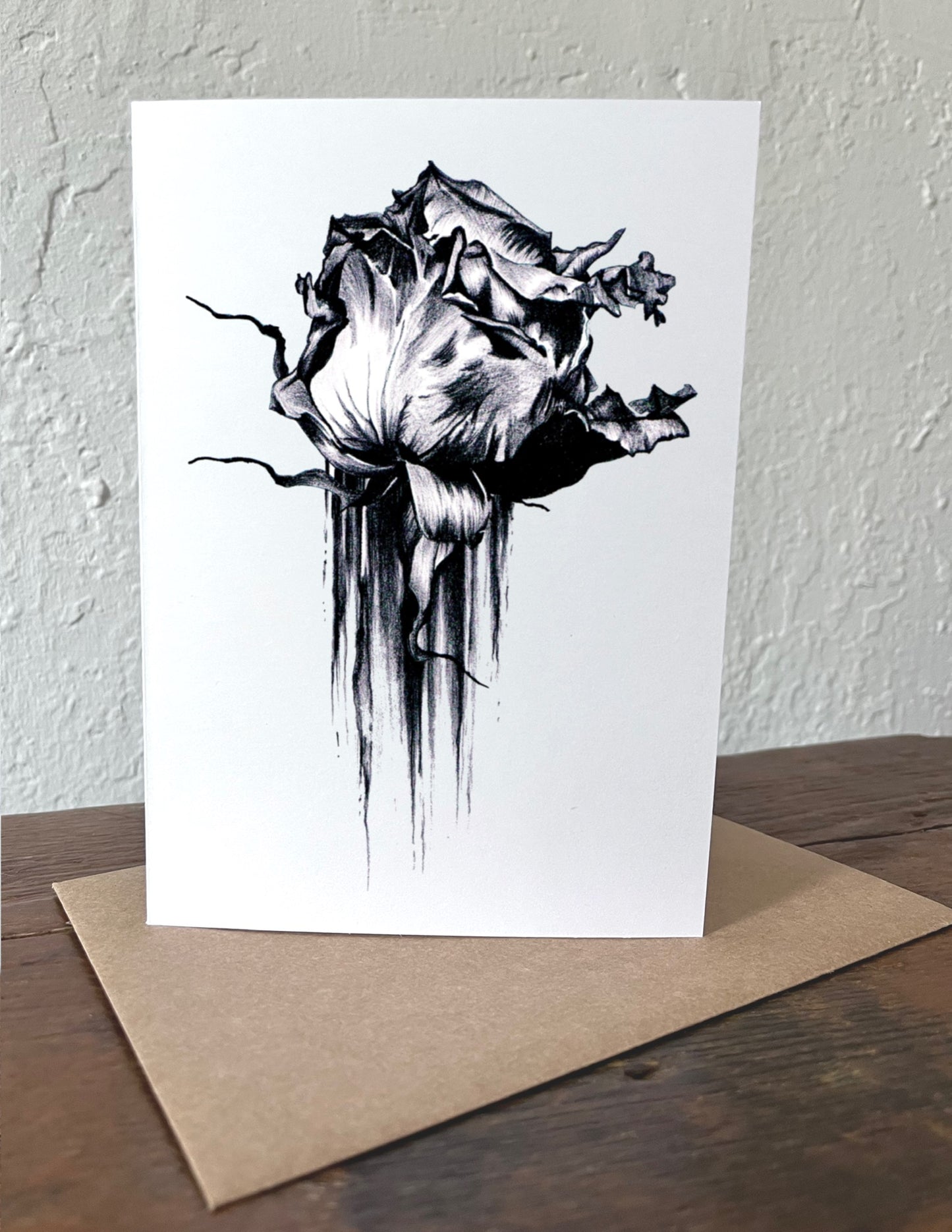 Greeting card with black and white rose design on a wooden surface with a beige envelope.