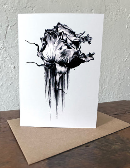 Greeting card with black and white rose design on a wooden surface with a beige envelope.