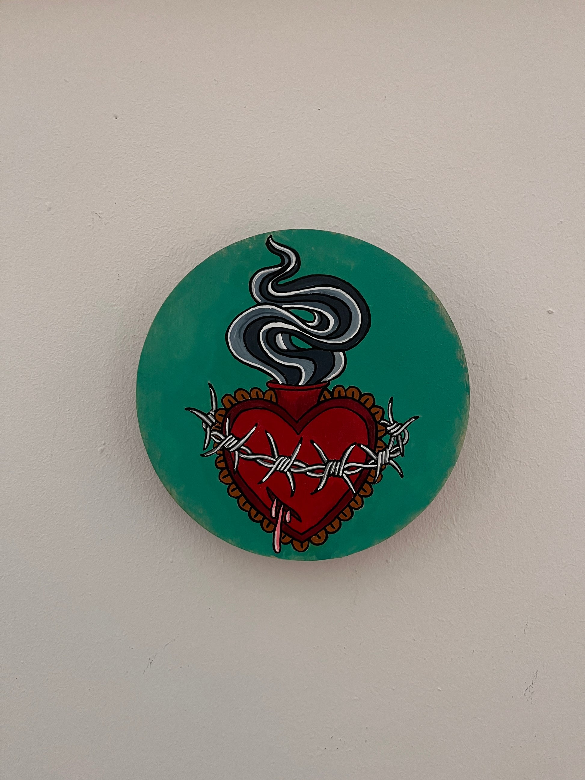 Round painting with a red heart and barbed wire design on a teal background