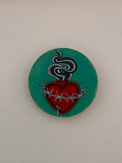 Round painting with a red heart and barbed wire design on a teal background
