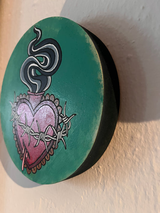 Teal wood panel with artistic designs of a scared heart and smoke wrapped in barbed wire on a beige background