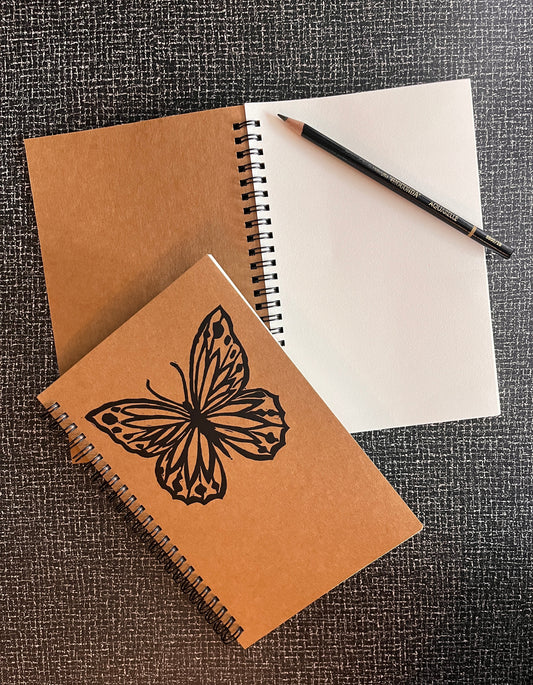 Brown notebook with butterfly design on cover, white paper, and black pen on textured surface
