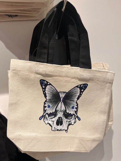 Beige tote bag with a butterfly skull design on a white surface