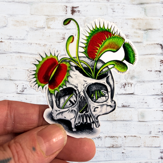 Skull with venus flytrap design held by a hand on a white wooden background