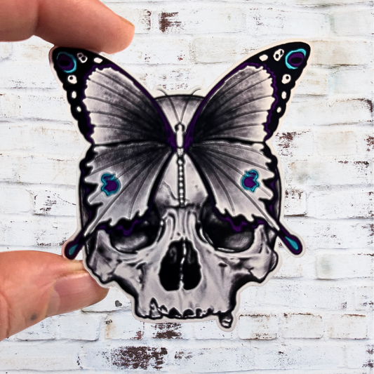 Butterfly skull design held by a hand against a white brick wall background