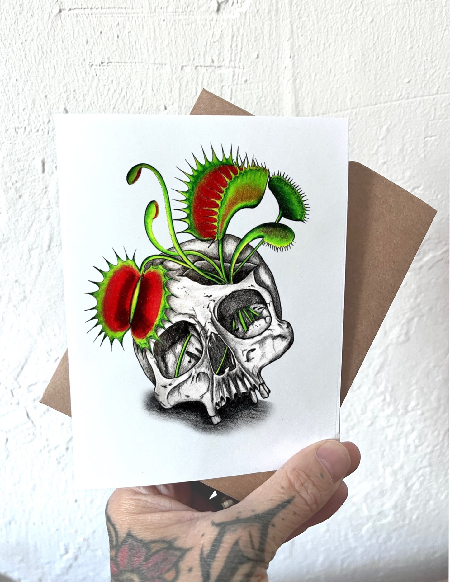 Card with a skull and Venus flytrap design held by a hand.