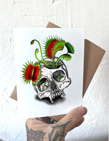 Card with a skull and Venus flytrap design held by a hand.