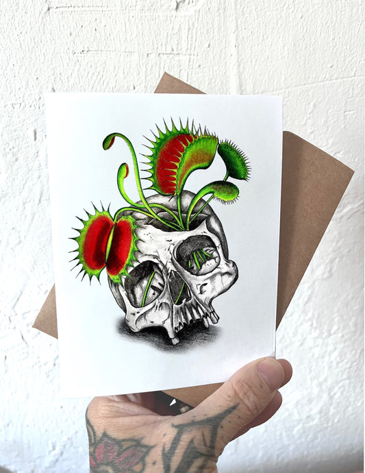 Card with a skull and Venus flytrap design held by a hand.