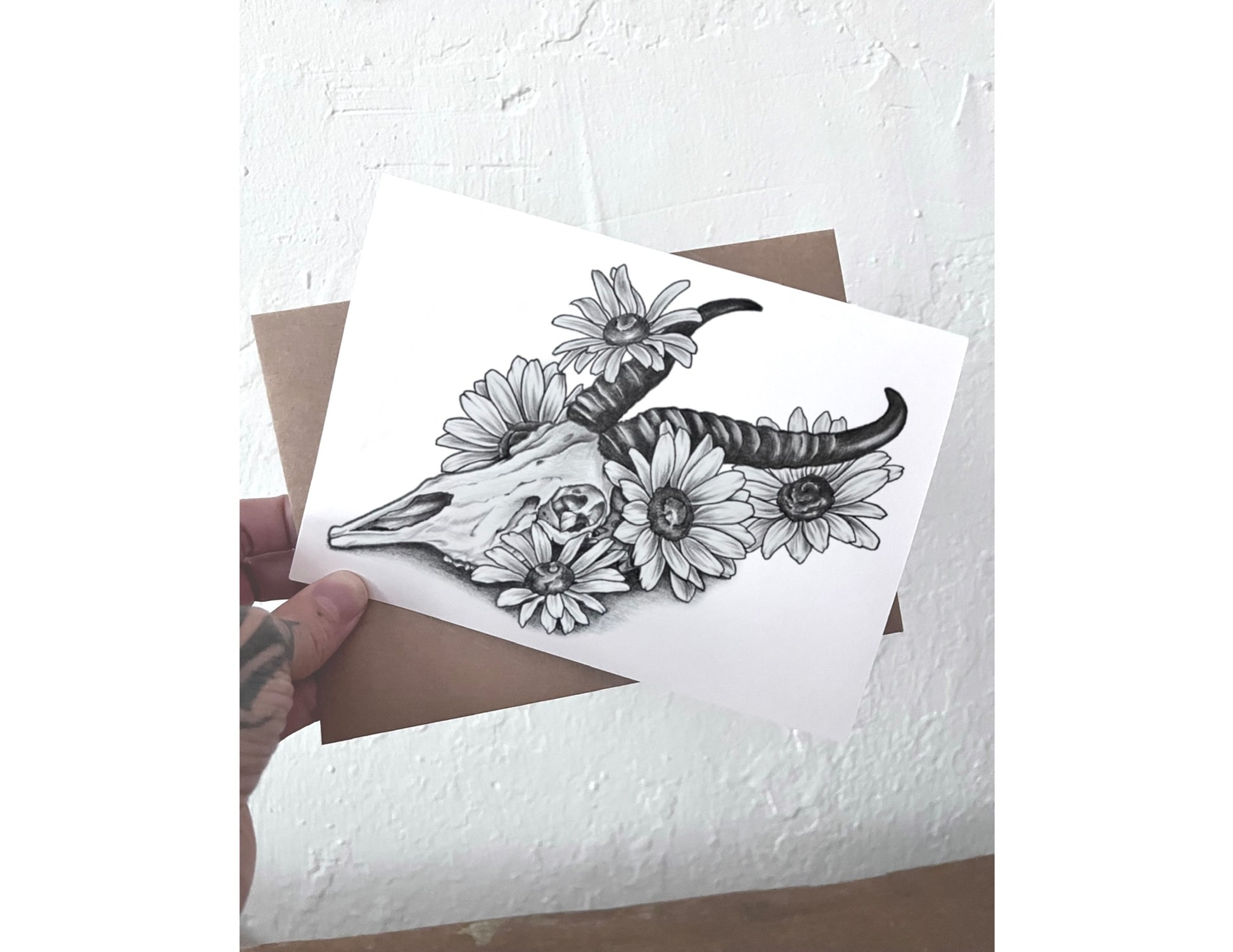 Card with black and white illustration of a skull and flowers held over an envelope.