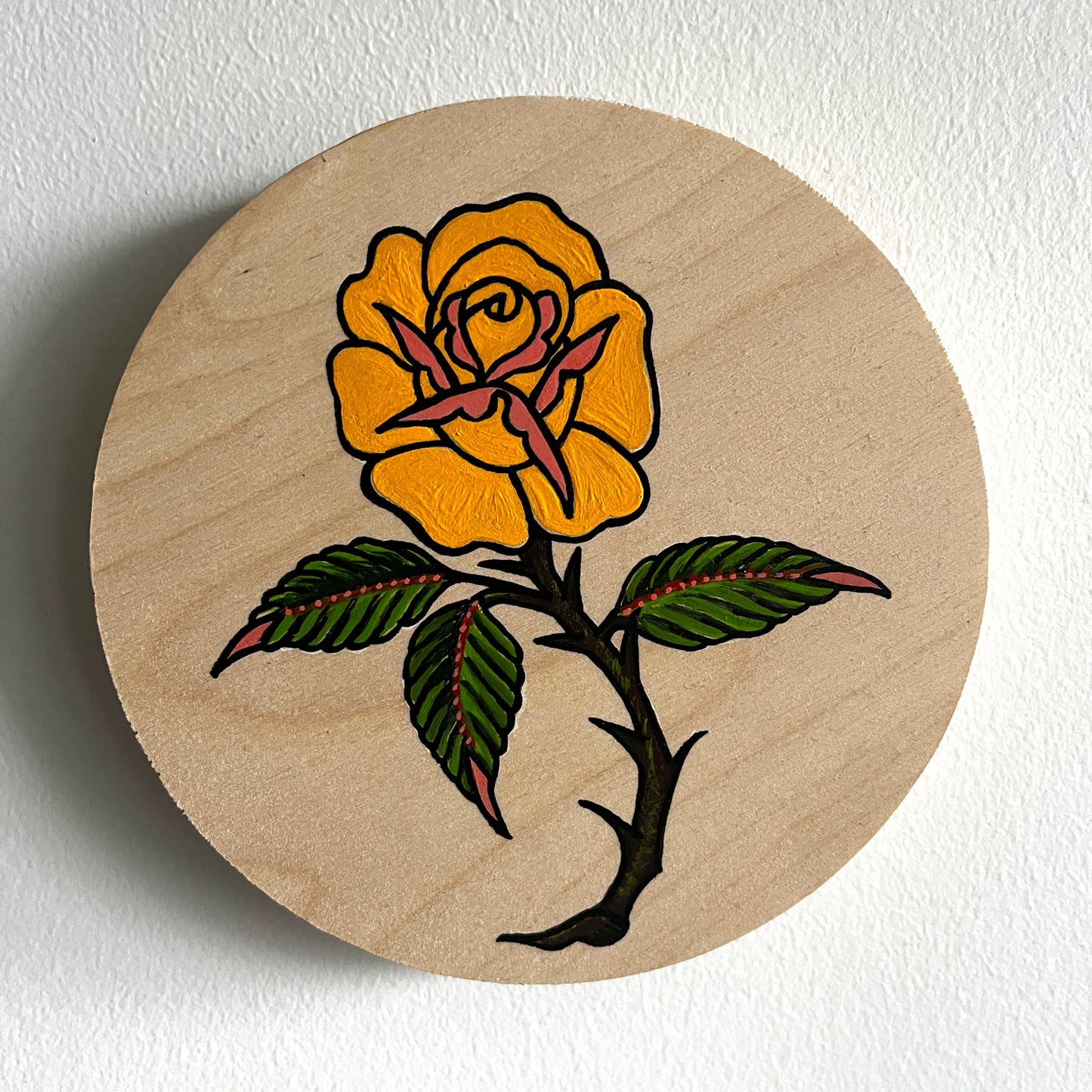 Round wooden painting with a traditional tattoo style yellow long stem rose design on a white background